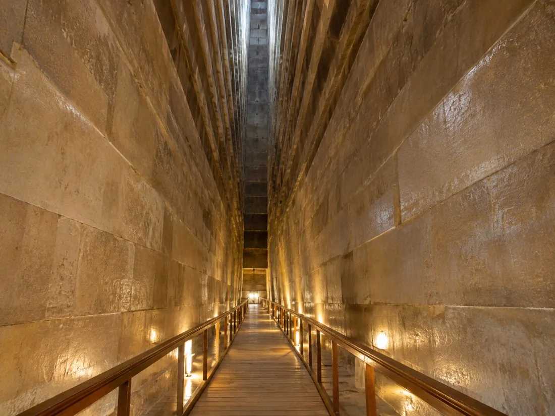 The tall corbelled Grand Gallery inside the Great Pyramid, lit by soft lamps along a steep wooden walkway