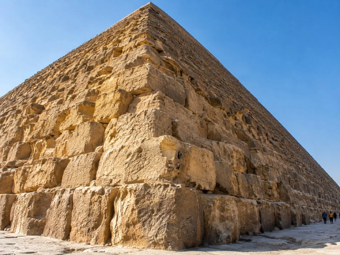 The huge limestone blocks at the base of the Great Pyramid of Khufu, with small figures of visitors for scale