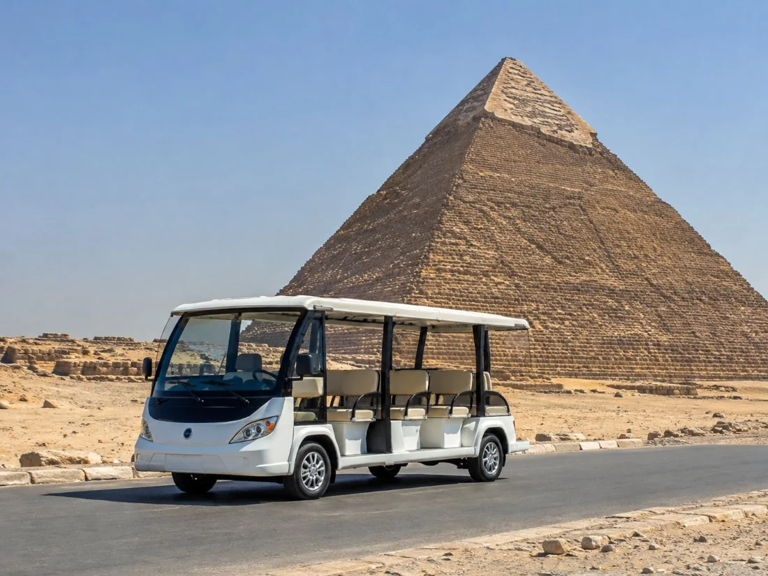 A white electric shuttle bus on the road across the Giza plateau with the Great Pyramid behind it
